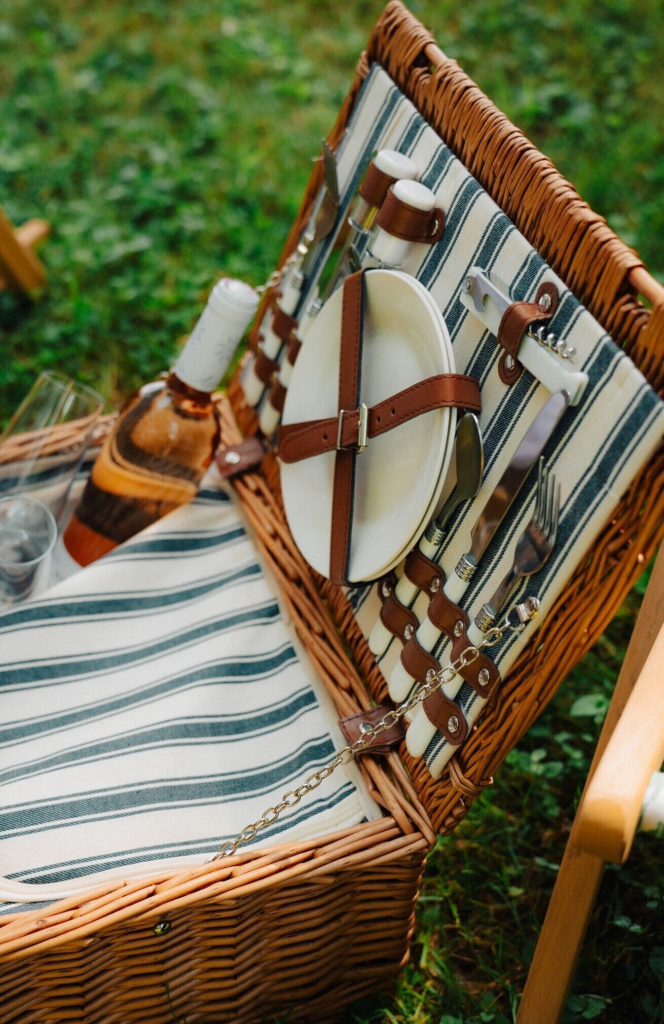 A wicker chair with a striped cushion, equipped with a bottle, glasses, and cutlery.