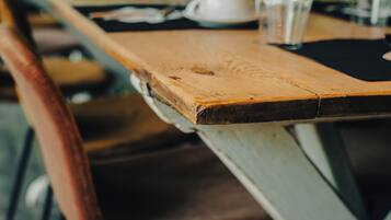 Una larga mesa de madera con sillas, en un espacio con fondo verde y desenfocado.