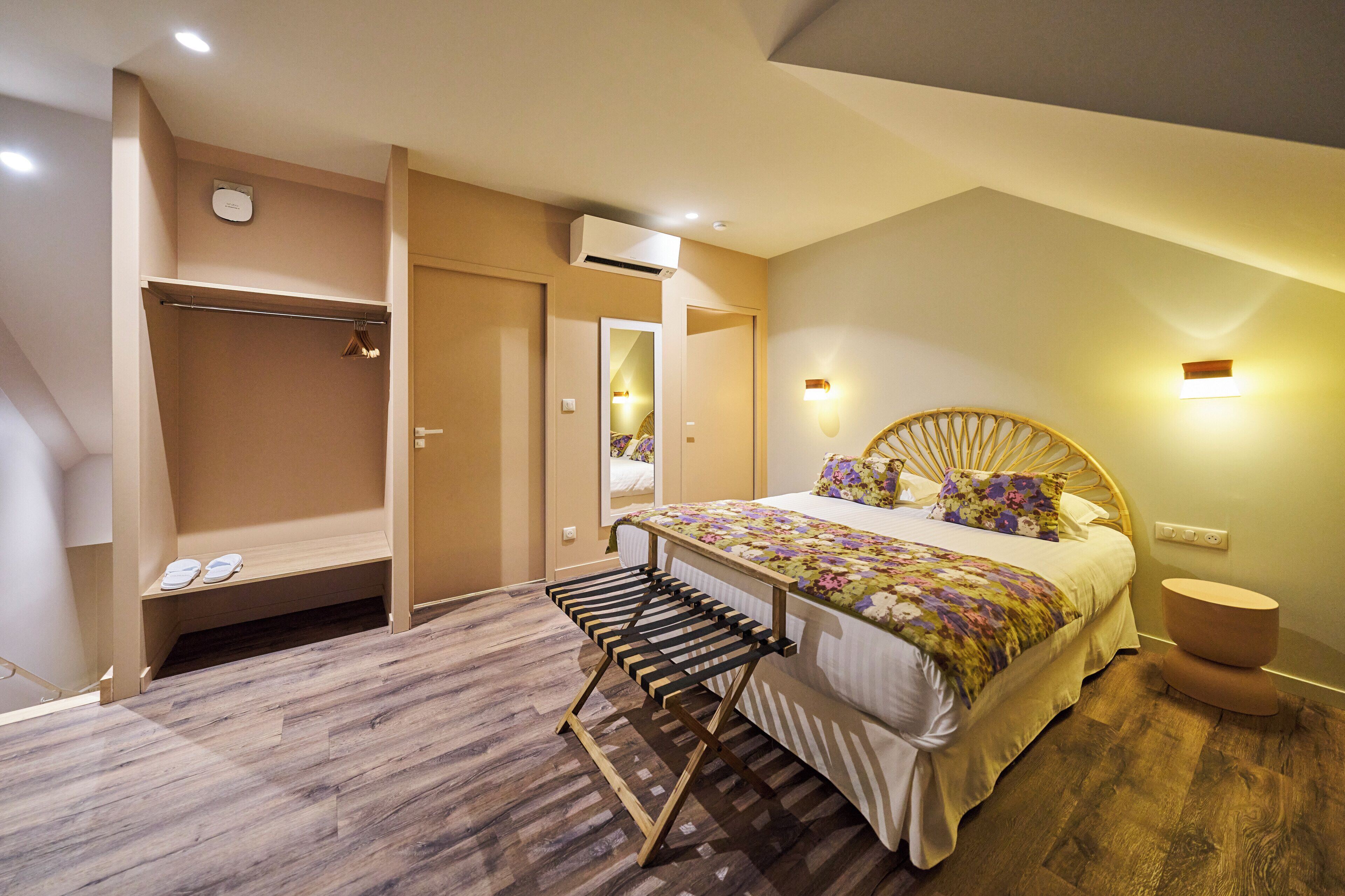 A bedroom with a bed, a wooden bench, a wardrobe, and a mirror.