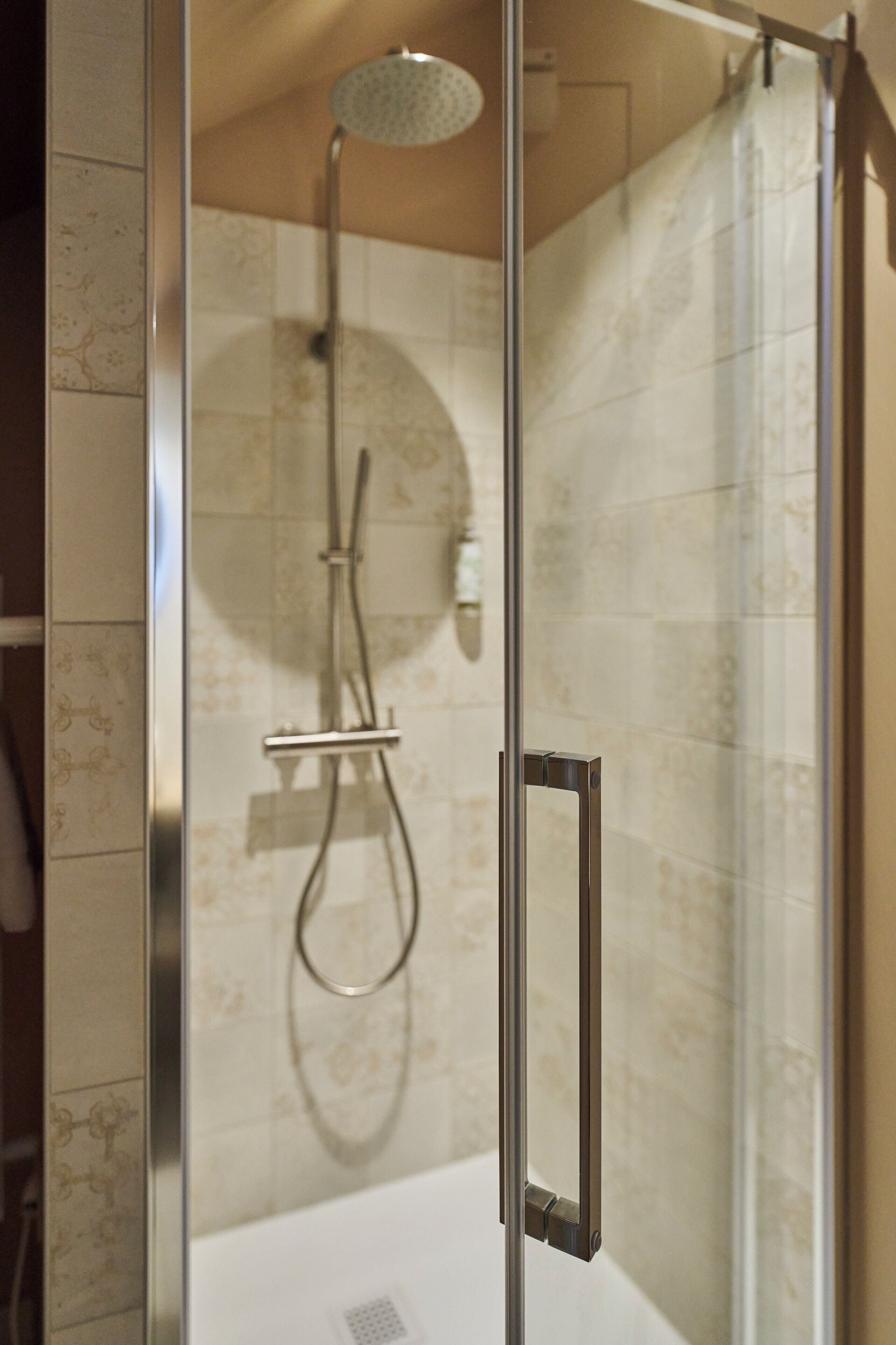 A glass-enclosed shower with a handheld showerhead and a fixed overhead showerhead.