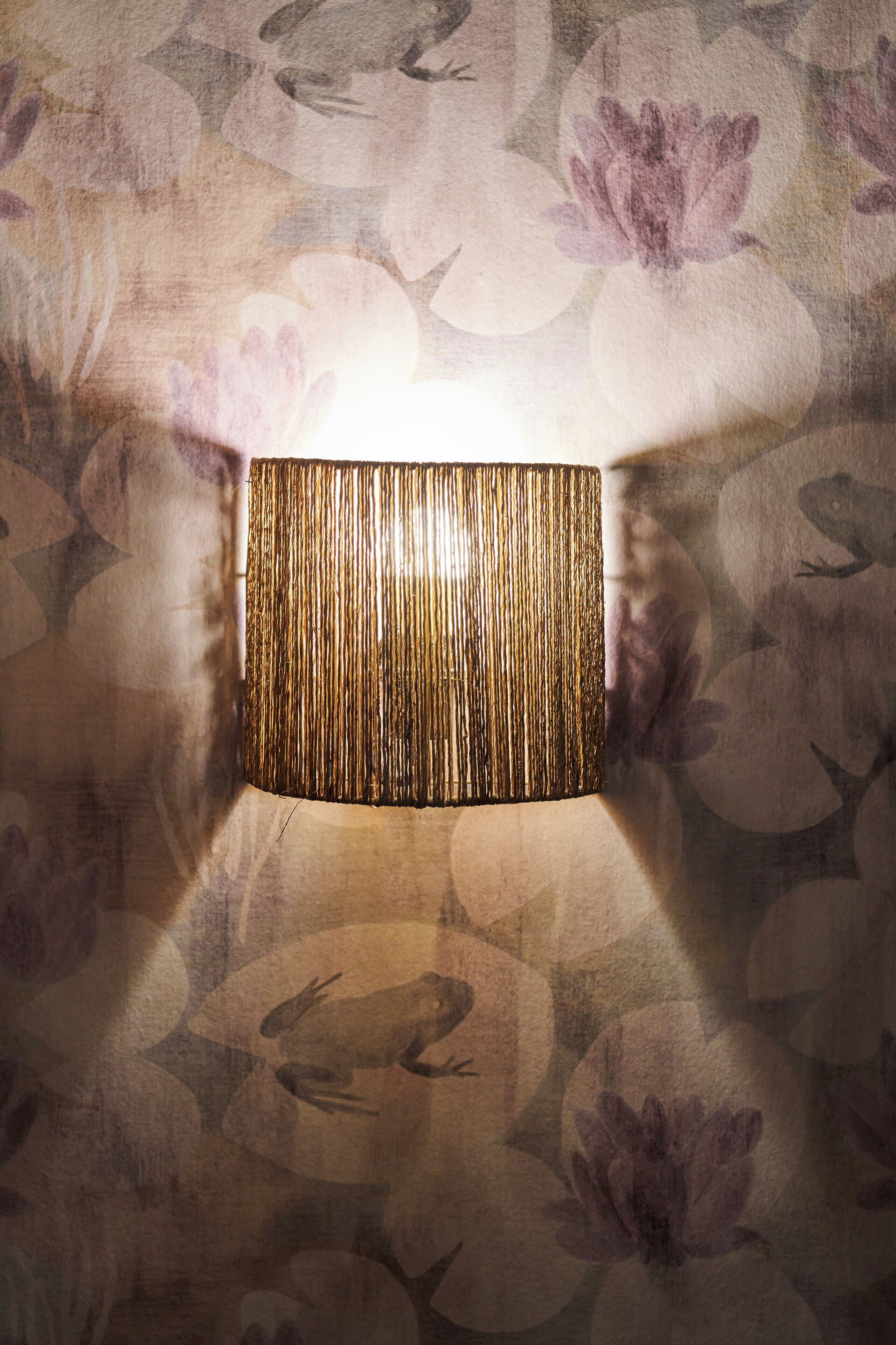 A wall-mounted lamp with a textured cylindrical shade against a floral wallpaper background.