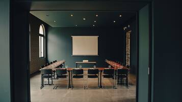 Un salón de conferencias con una larga mesa, sillas, una pantalla de proyector y una pared de ladrillo.