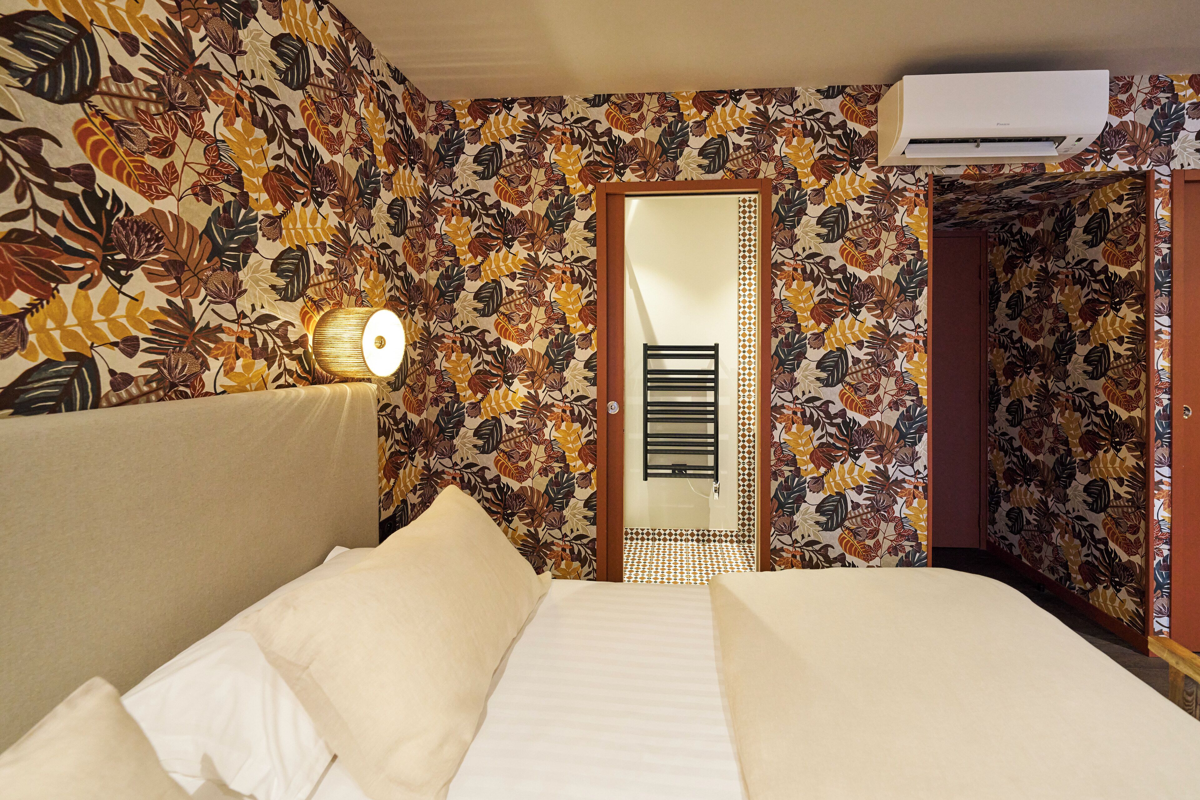 Una habitación de hotel con cama, aire acondicionado instalado en la pared y una puerta con espejo decorativo.