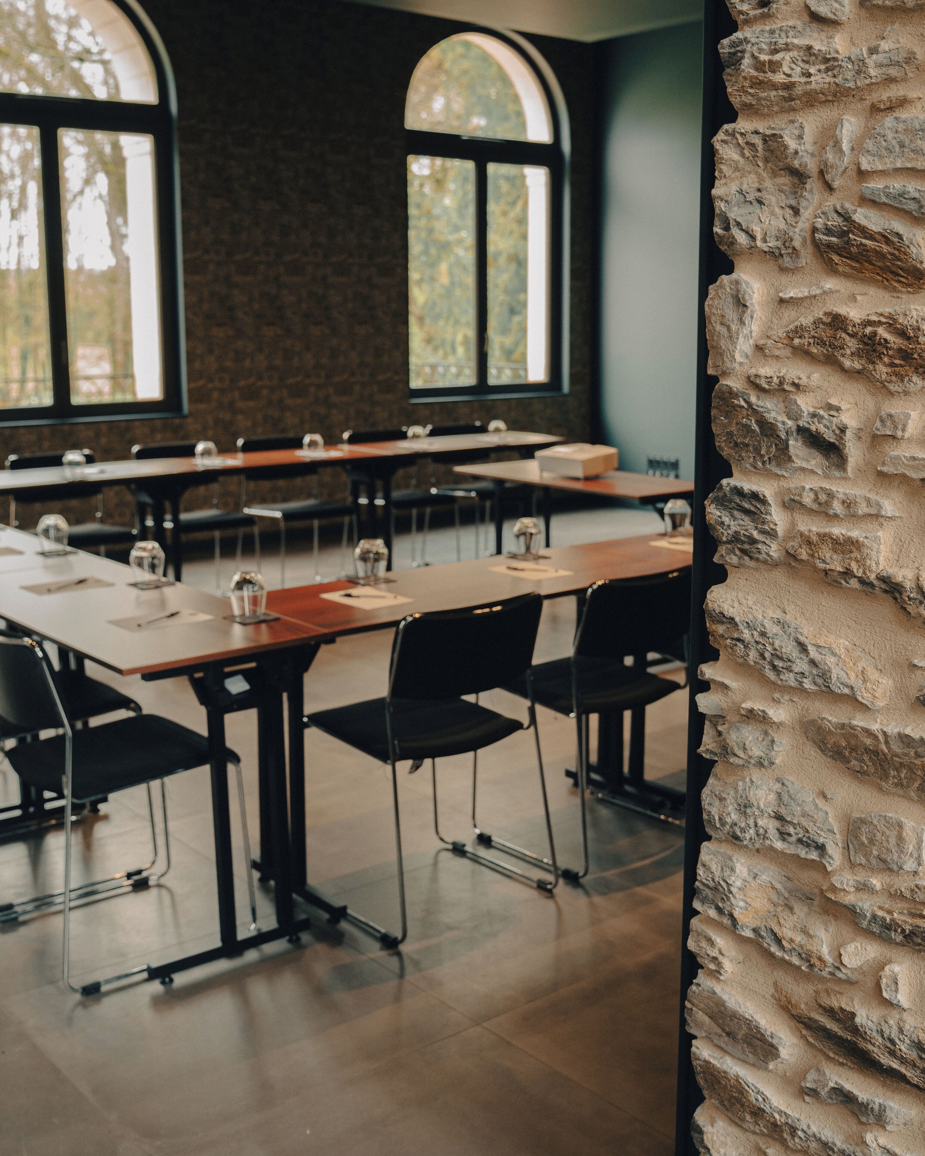 Un salón de conferencias con mesas largas, sillas negras y una pared de piedra.