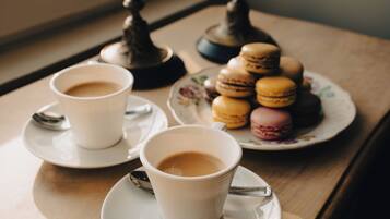 Two cups of coffee on a table with a plate of macarons and a spoon.