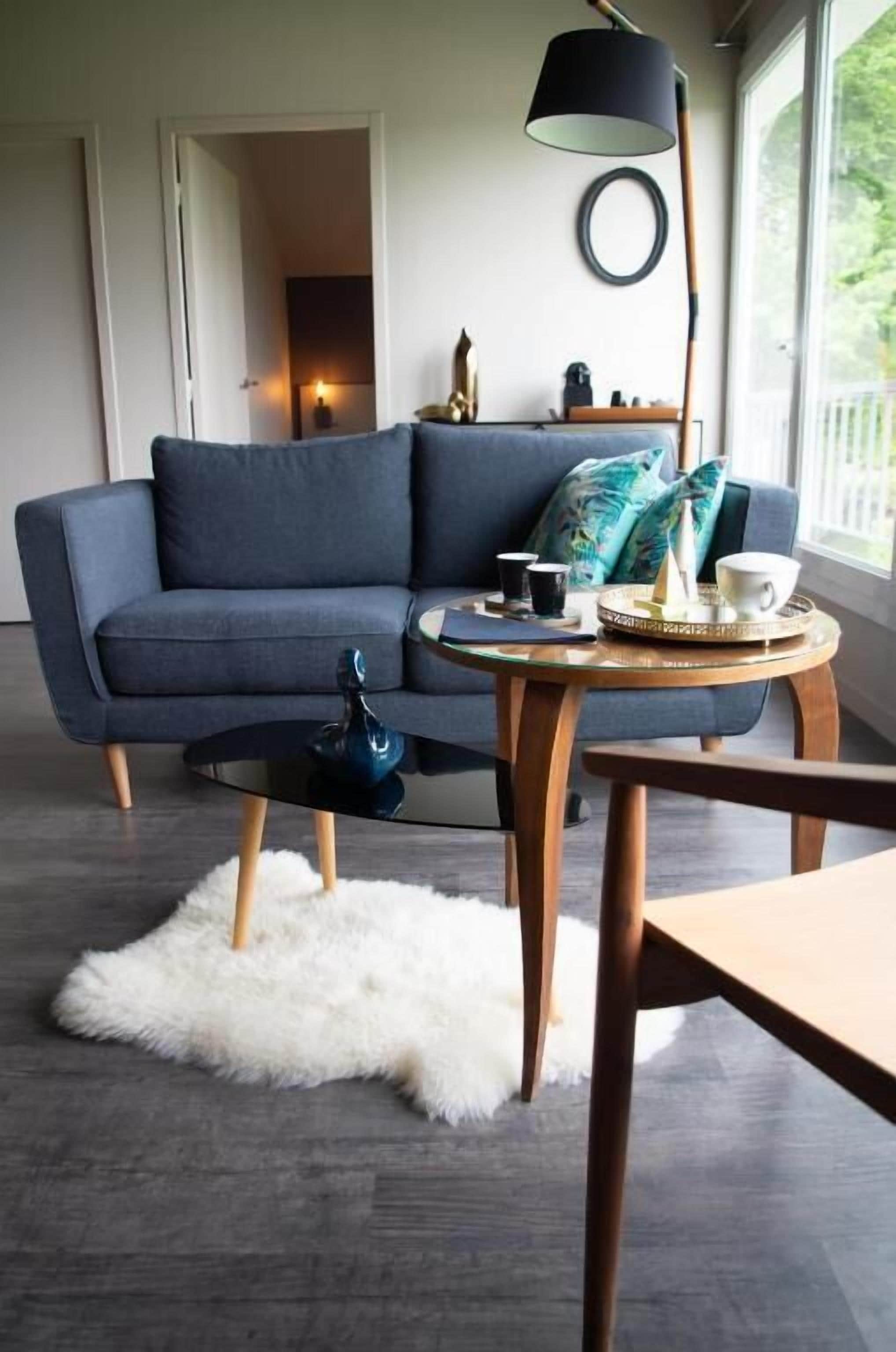 Un salon moderne avec un canapé bleu foncé, une table basse ronde, un tapis blanc à poils longs et une lampe.