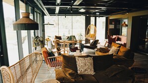 A modern interior with a brown sofa, wicker chairs, and a dining area with a table and chairs. - Hôtel Le Corbusson Laval Ouest (Saint-Berthevin)