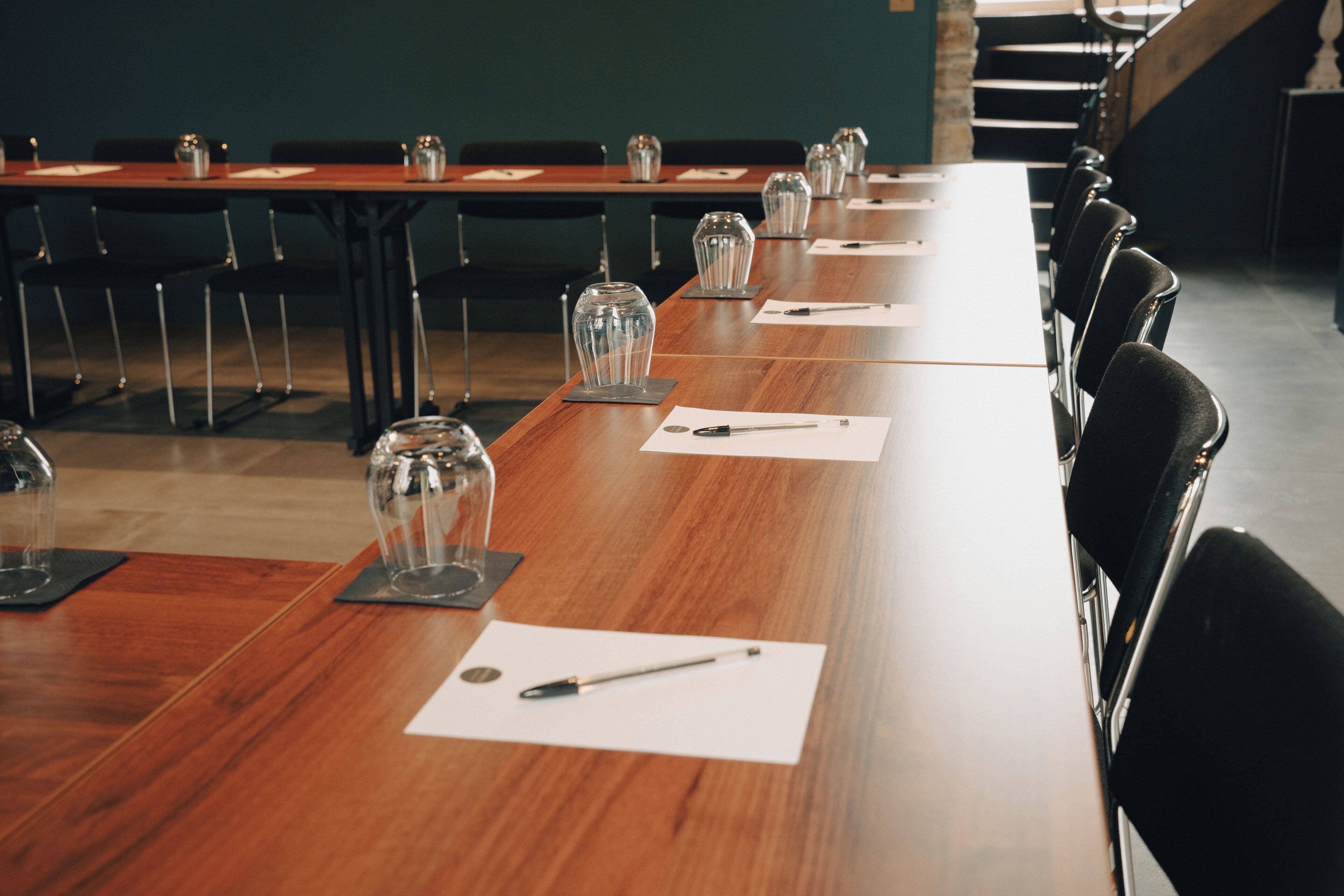 Une salle de conférence avec de longues tables, des chaises et de la verrerie sur chaque table.