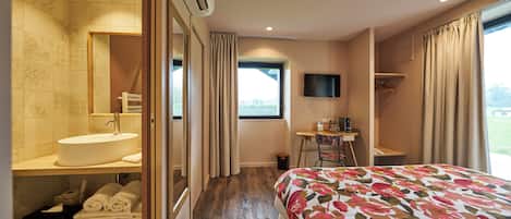 Una camera d'albergo con un letto grande, un bagno con lavandino e specchio, una TV e una finestra con tende.
