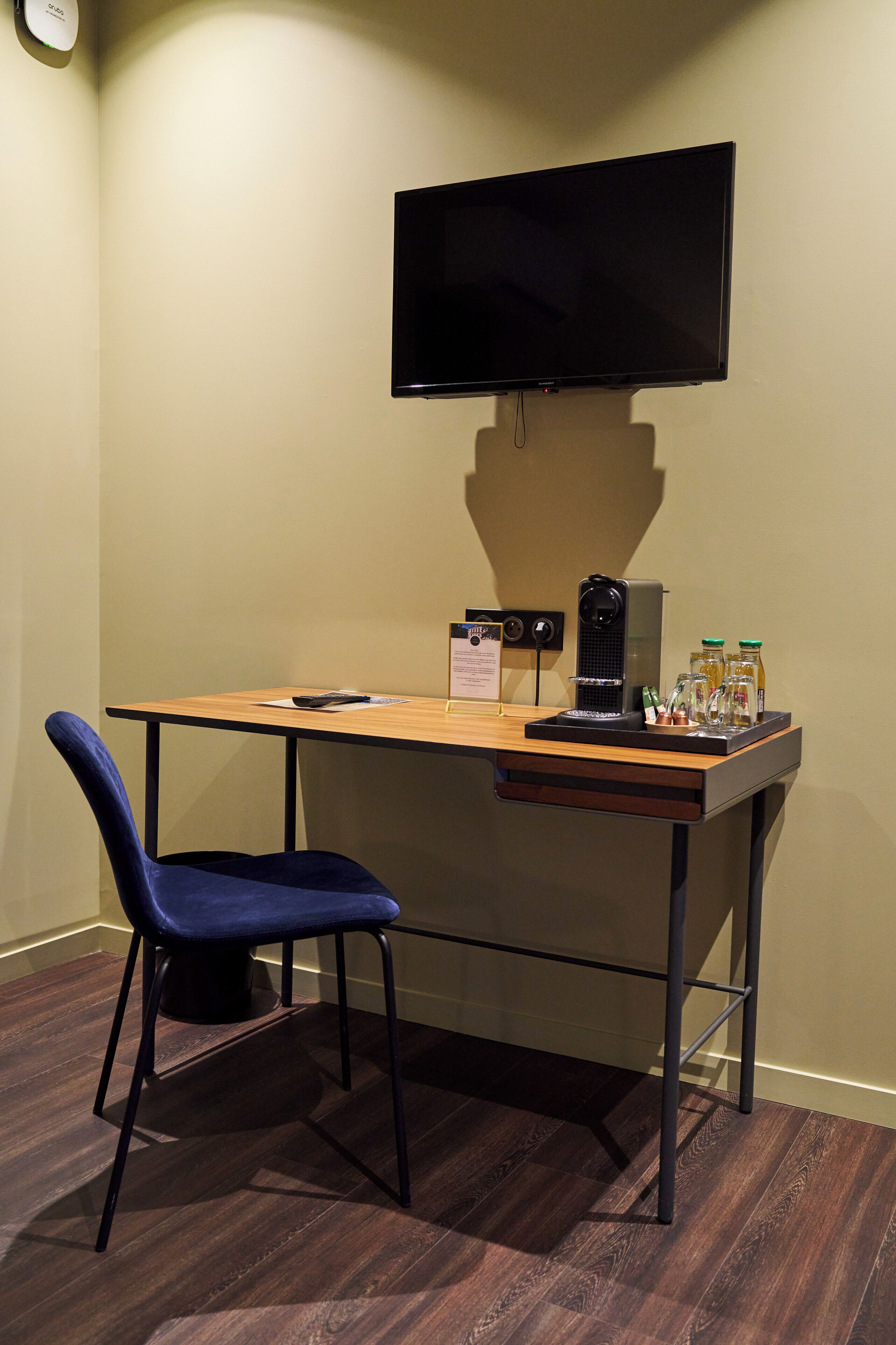 A small office space with a desk, chair, flat-screen TV, and a speaker.
