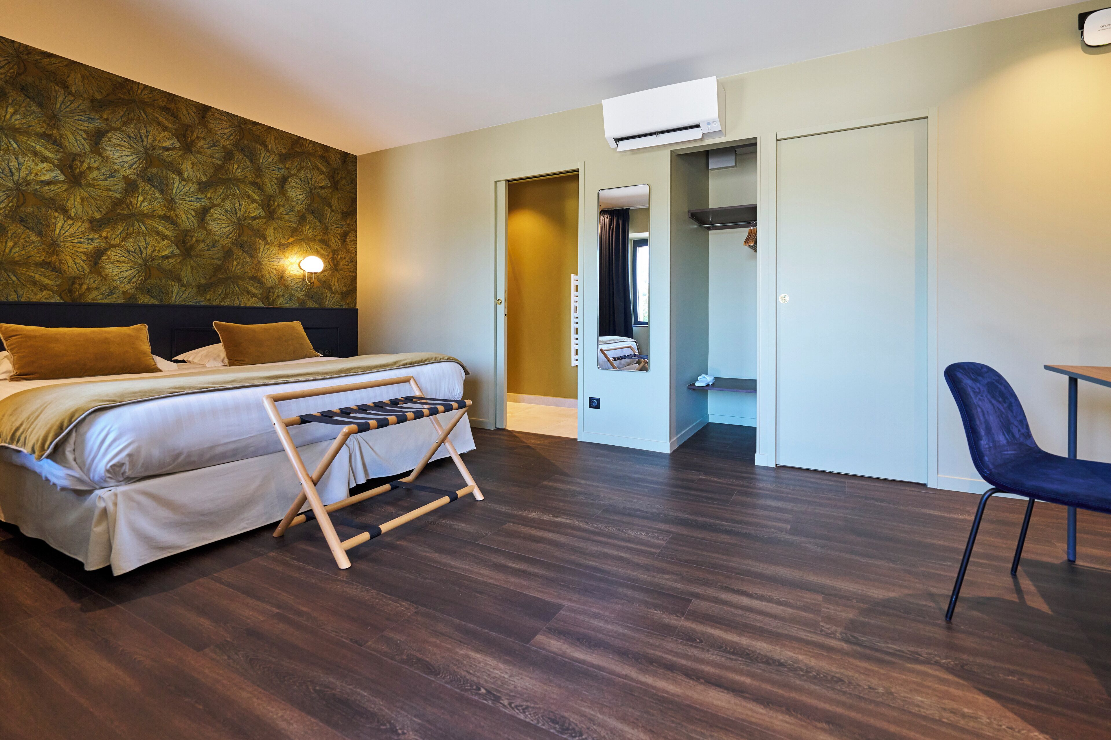 Habitación de hotel con cama, suelo de madera, una silla, armario y espejo.