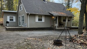 A two-story house with a covered porch, a chimney, and a small front yard with scattered leaves.