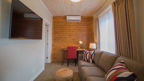 A cozy room with a wooden wall, a sofa, a small table, and a chair. - Cranberry Arms Inn (Cassidy)