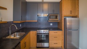 A modern kitchen with grey cabinets, a stainless steel sink, a built-in oven, a microwave, and a refrigerator. - Cranberry Arms Inn (Cassidy)