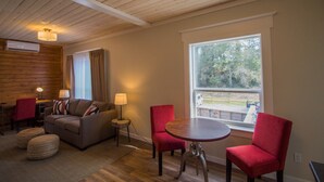A cozy living room with a sofa, two red chairs, a round table, and a large window offering a view of the outdoors. - Cranberry Arms Inn (Cassidy)