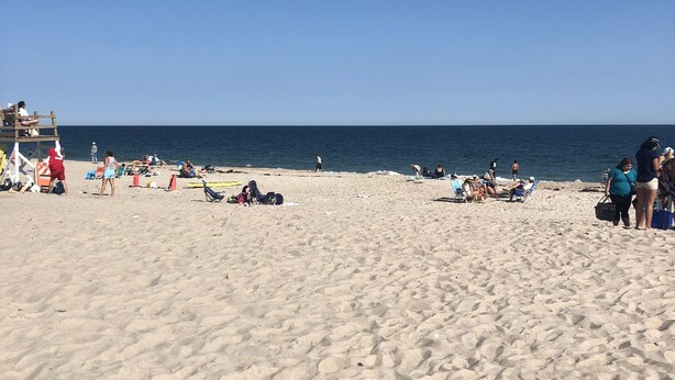 Una playa arenosa con gente tomando el sol y paseando.