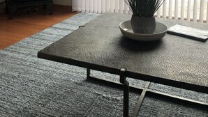 Una sala de estar con chimenea, un ventanal con persianas, un tapete texturizado y una planta en maceta.