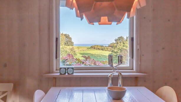 Una habitación con ventana que da a un paisaje, una mesa con un cuenco y un estante pequeño con dos relojes.