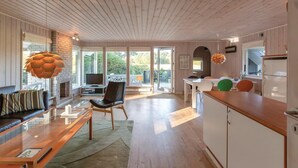 Una cocina moderna con armarios blancos, encimera de madera y horno empotrado. Hay un comedor con mesa y sillas, y una sala de estar con sofá y chimenea.