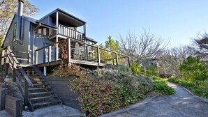 A modern two-story house with a wooden deck and stairs leading to a balcony. - Cloudsong Chalet 1 - Close to the village centre! (Kangaroo Valley)