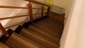 A wooden staircase with a handrail, leading to a landing with a yellow wall and a brick wall. - Yi-Jing B&B (Hualien City)