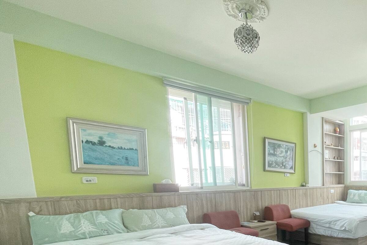 Ett hotellrum med en stor säng, en soffa, ett skrivbord och en stol. Det finns två fönster och en takfläkt.