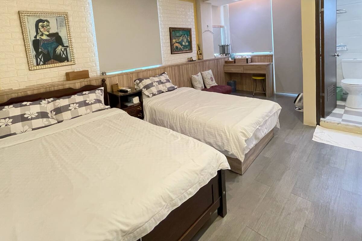 Ett hotellrum med två sängar, en sänggavel i trä, ett litet skrivbord, en spegel och ett badrum med toalett och handfat.