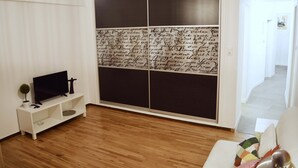 Ett modernt vardagsrum med en platt-TV på ett vitt TV-bord, en liten krukväxt och en stor skjutdörr med en svartvit, abstrakt design.