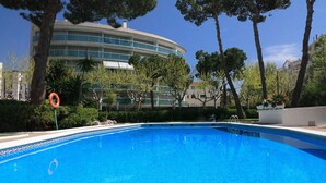 Ein Schwimmbecken mit klarem, blauem Wasser, umgeben von Bäumen und einem modernen Gebäude mit Balkonen.