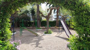 Ein Spielplatz mit Rutschen und Klettergerüsten, umgeben von Bäumen und Grün.