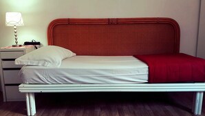 A bed with a white mattress and a red blanket, a bedside lamp, and a white nightstand with drawers. - Roman Place (Rome)