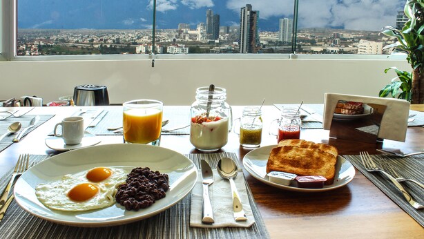 A breakfast table with eggs, beans, toast, and a view of a cityscape through a window. - Lâviu B&B Luxe Suites (San Andrés Cholula)