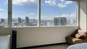 A room with a large window offering a city view, a bed, a chair, and a radiator. - Lâviu B&B Luxe Suites (San Andrés Cholula)