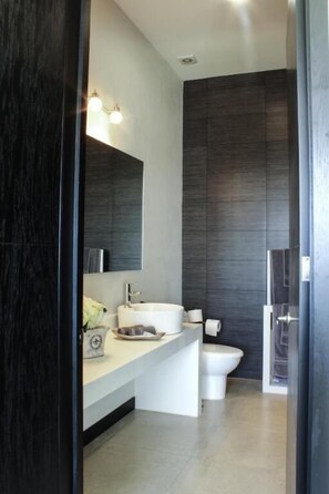 A modern bathroom with a dark wood vanity, a white sink, a mirror, and a toilet. - Lâviu B&B Luxe Suites (San Andrés Cholula)