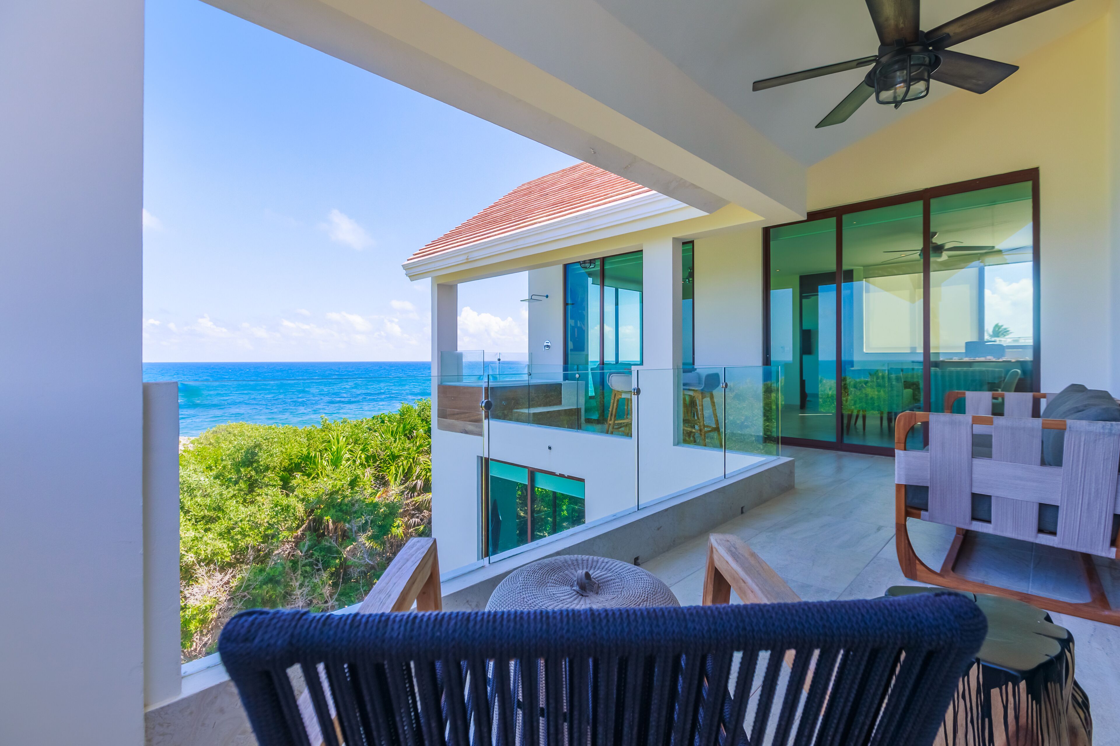 A modern balcony with a view of the ocean, a ceiling fan, and a dining area with a table and chairs.