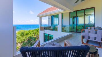 A modern balcony with a view of the ocean, a ceiling fan, and a dining area with a table and chairs.