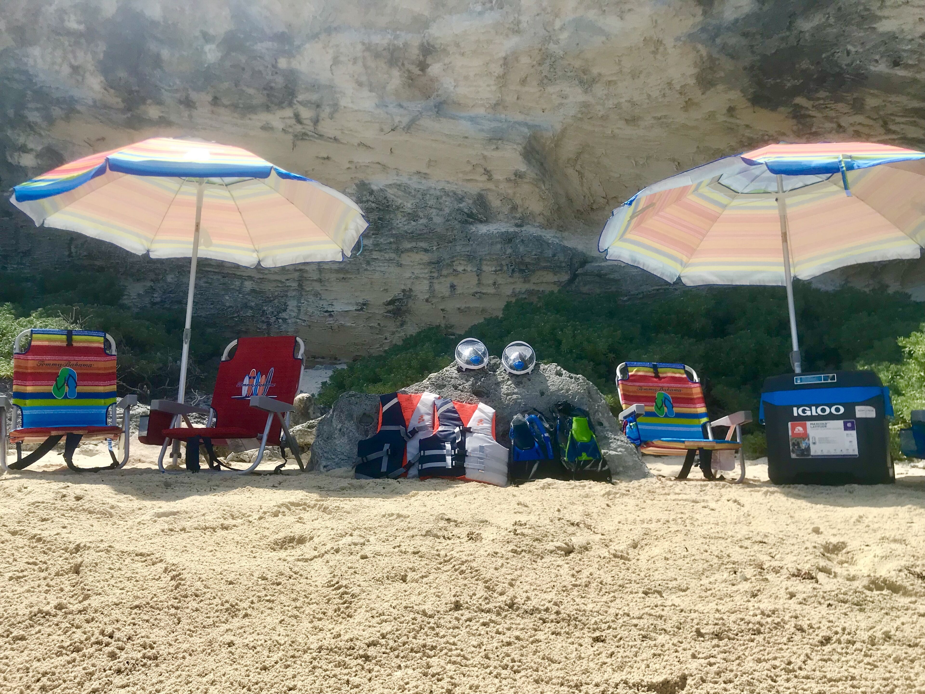 A beach with two umbrellas, beach chairs, and a sandcastle.