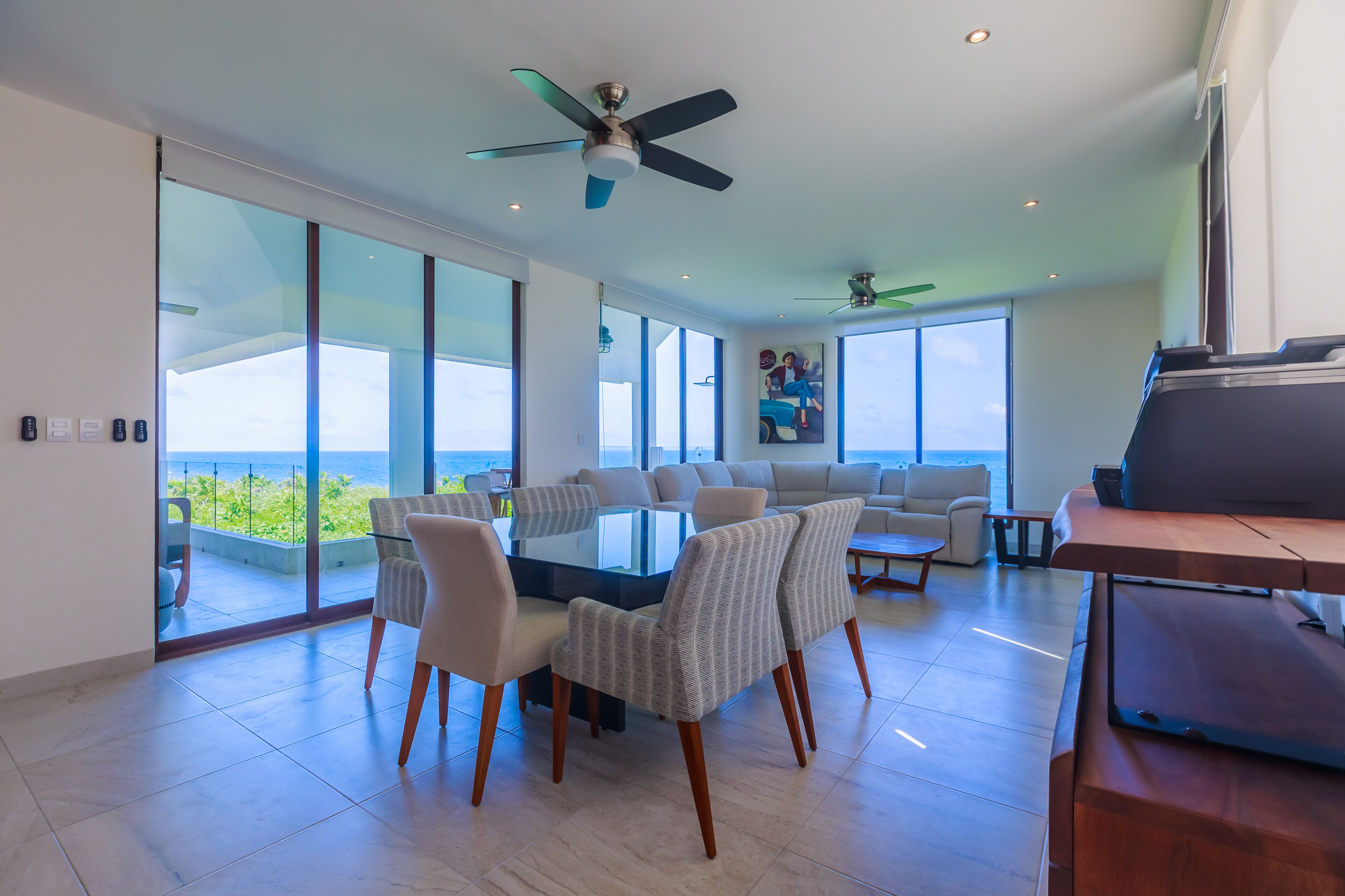 A spacious living area with a glass table surrounded by chairs, a sofa, and a ceiling fan.