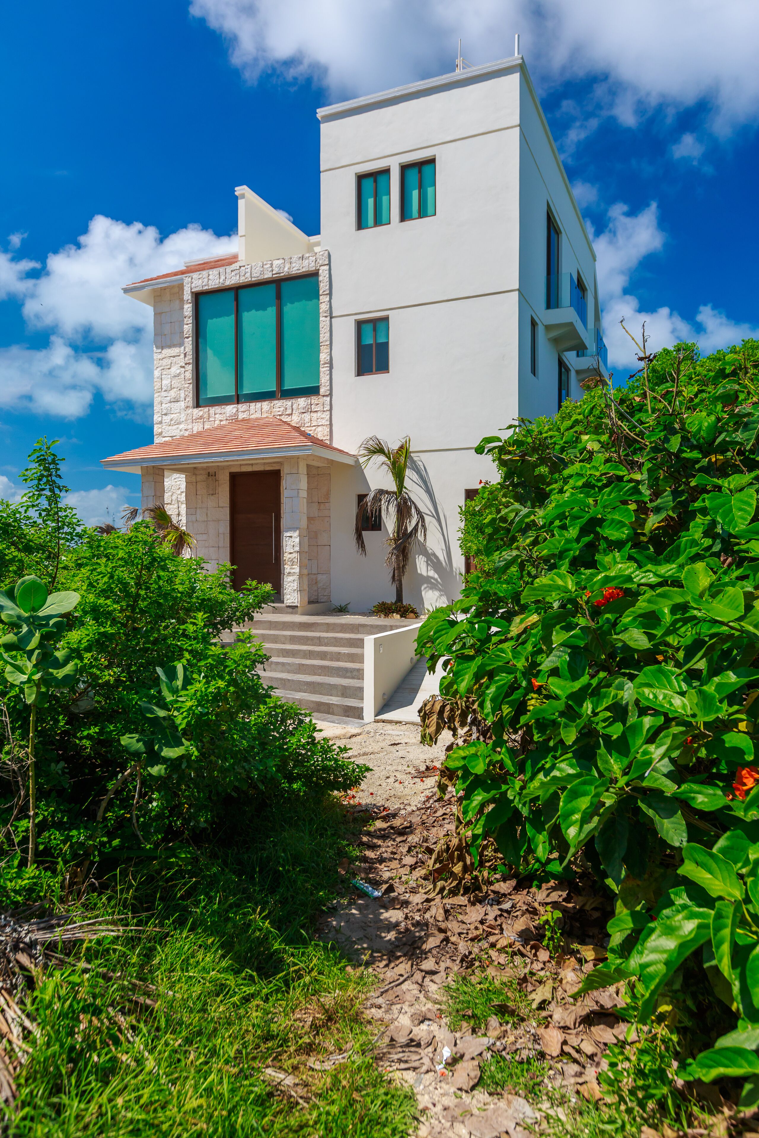A modern two-story house with a stone facade, large windows, and a red-tiled roof.