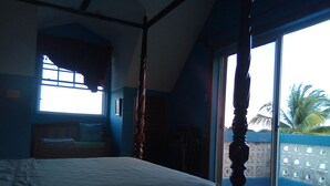 A bedroom with a large bed, a window, and a view of a palm tree. - Tropickeas (St. George's Caye)