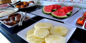 Un bufé con distintos alimentos, incluyendo sandía en rodajas, piña y salchichas.