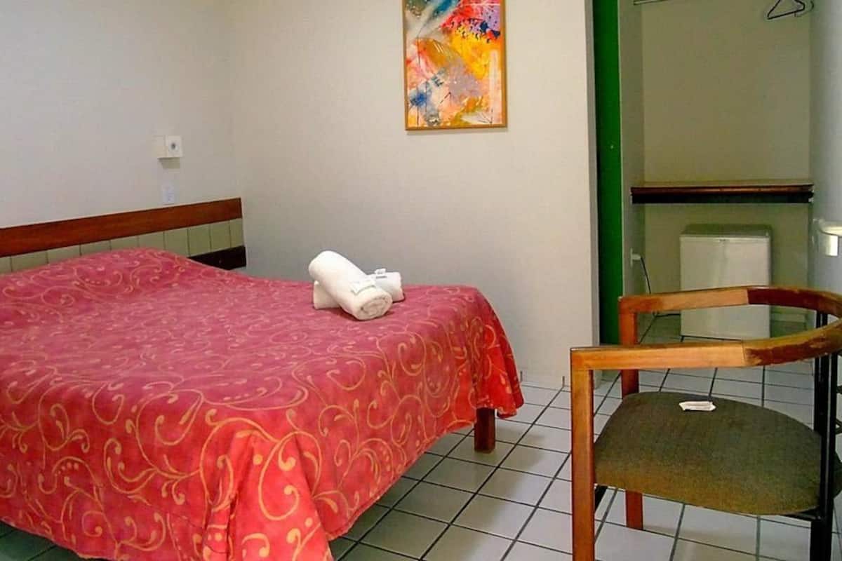 Ein Hotelzimmer mit Bett, einem Sessel, einem farbenfrohen Bild an der Wand und einer kleinen Küchenzeile.