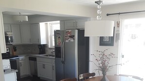 A kitchen with white cabinets, a refrigerator, a dining table with chairs, and a vase on the table.