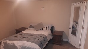A bedroom with a bed, nightstands, a door labeled "BATHROOM", and a carpeted floor.