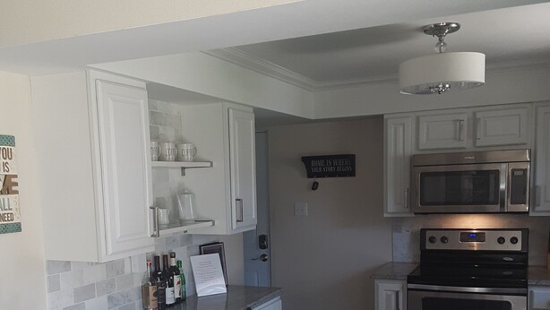A kitchen with white cabinets, a microwave, an oven, a bar stool, and a sign on the wall.