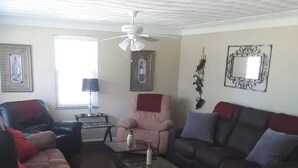 A living room with a brown leather sofa, a red and black armchair, a glass coffee table, and a ceiling fan.