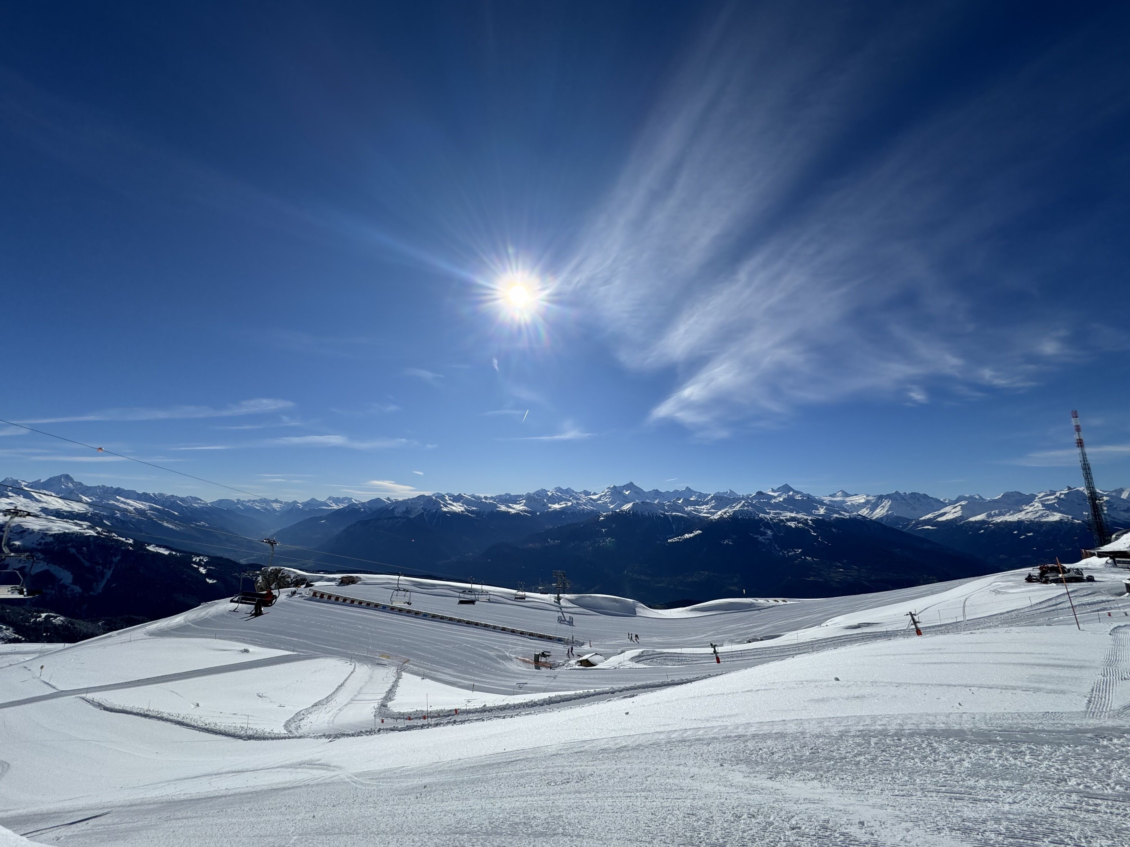 A snowy ski slope with ski lifts and a mountain range in the background.