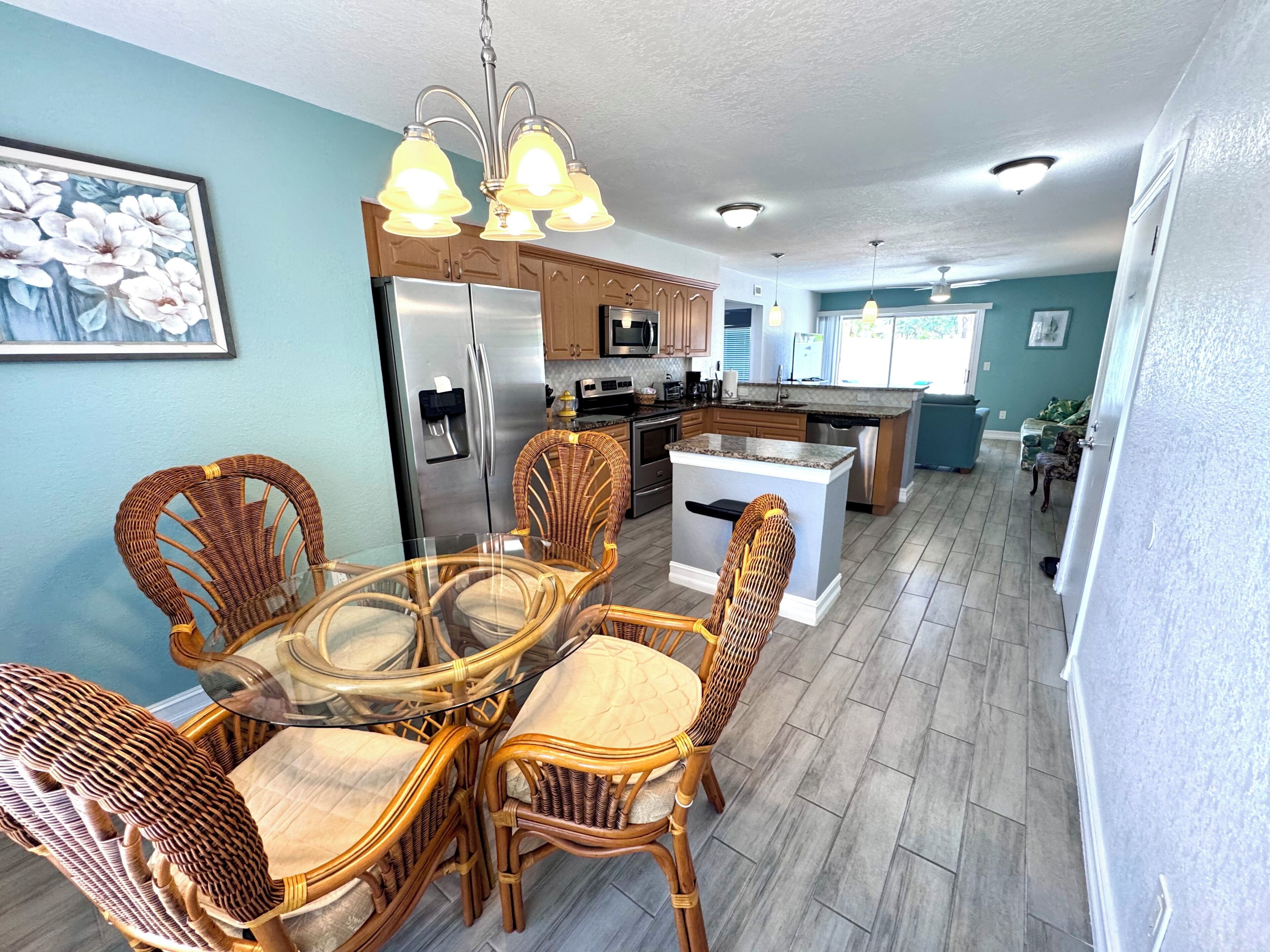 A modern kitchen with a central island, stainless steel appliances, and wicker chairs around a glass table.