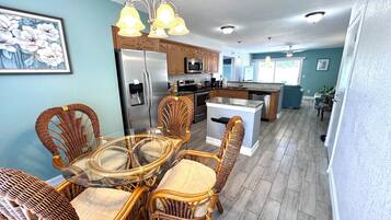 A modern kitchen with a central island, stainless steel appliances, and wicker chairs around a glass table.