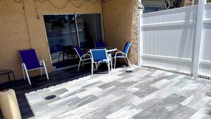 A patio with a herringbone tile floor, outdoor furniture, and a white fence.